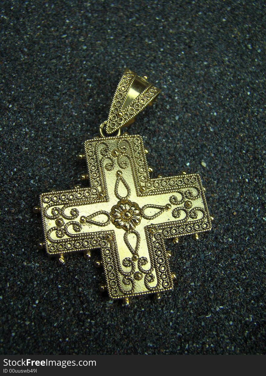 Antique golden cross jewel lying in black sand