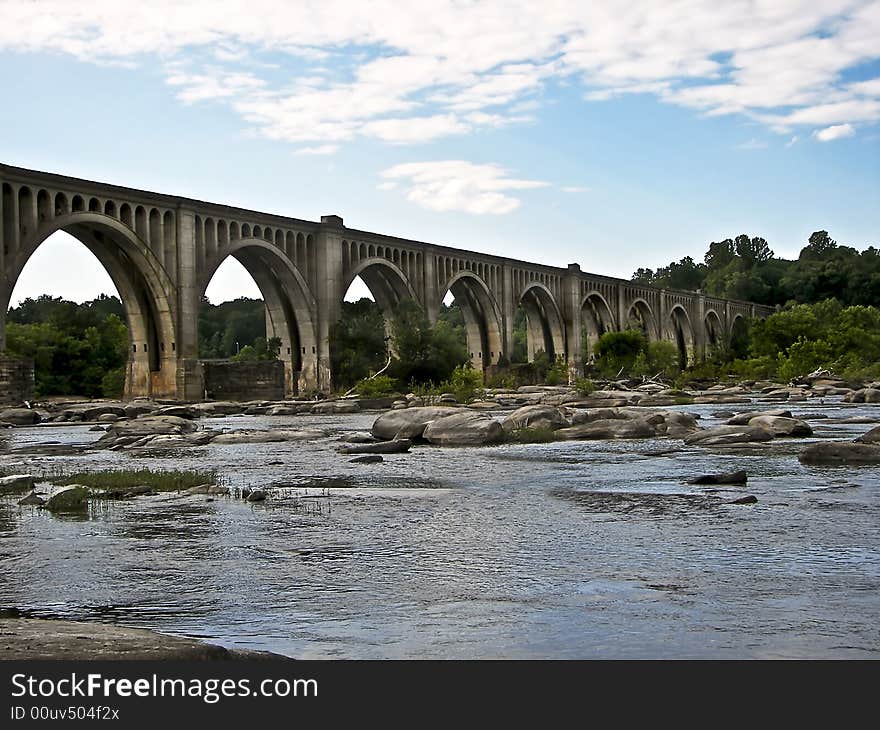 Old railroad bridge crossing a river with cloudy sky above and colorful water.