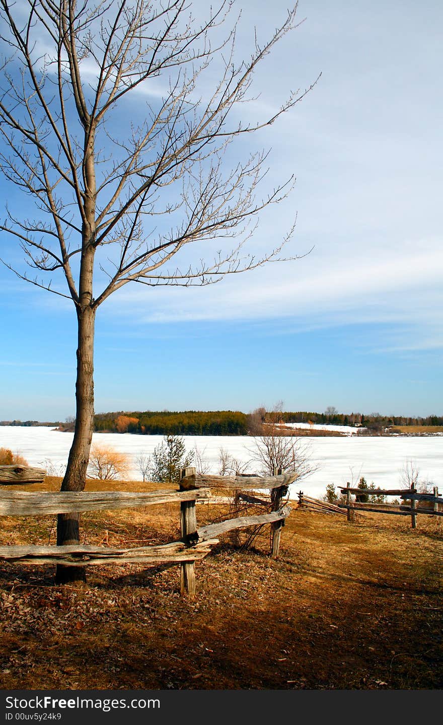 A fence leading to a frozen lake under a blue sky. A fence leading to a frozen lake under a blue sky