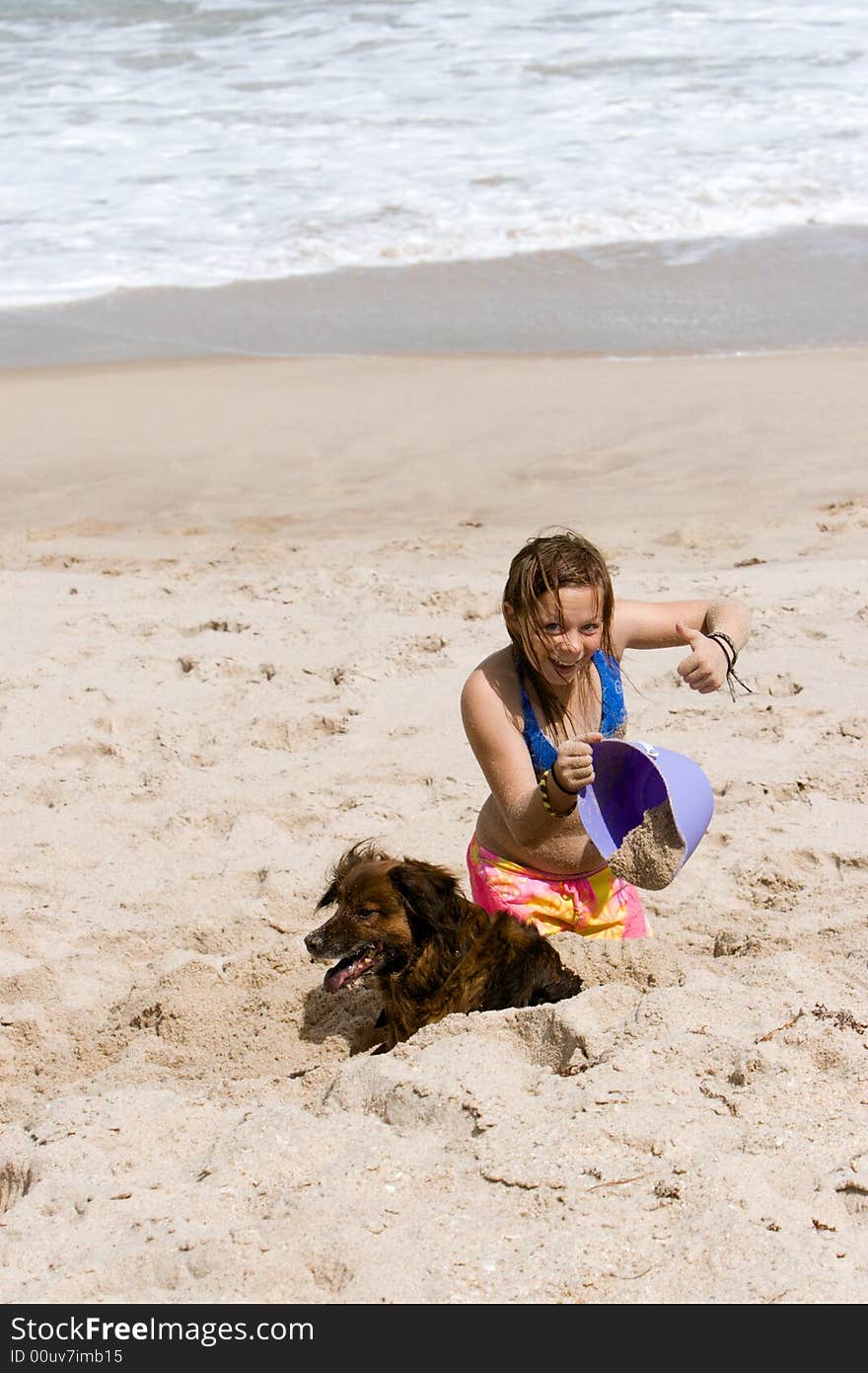 Young girl playing on the beach in the sand with a purple bucket and her dog. Young girl playing on the beach in the sand with a purple bucket and her dog