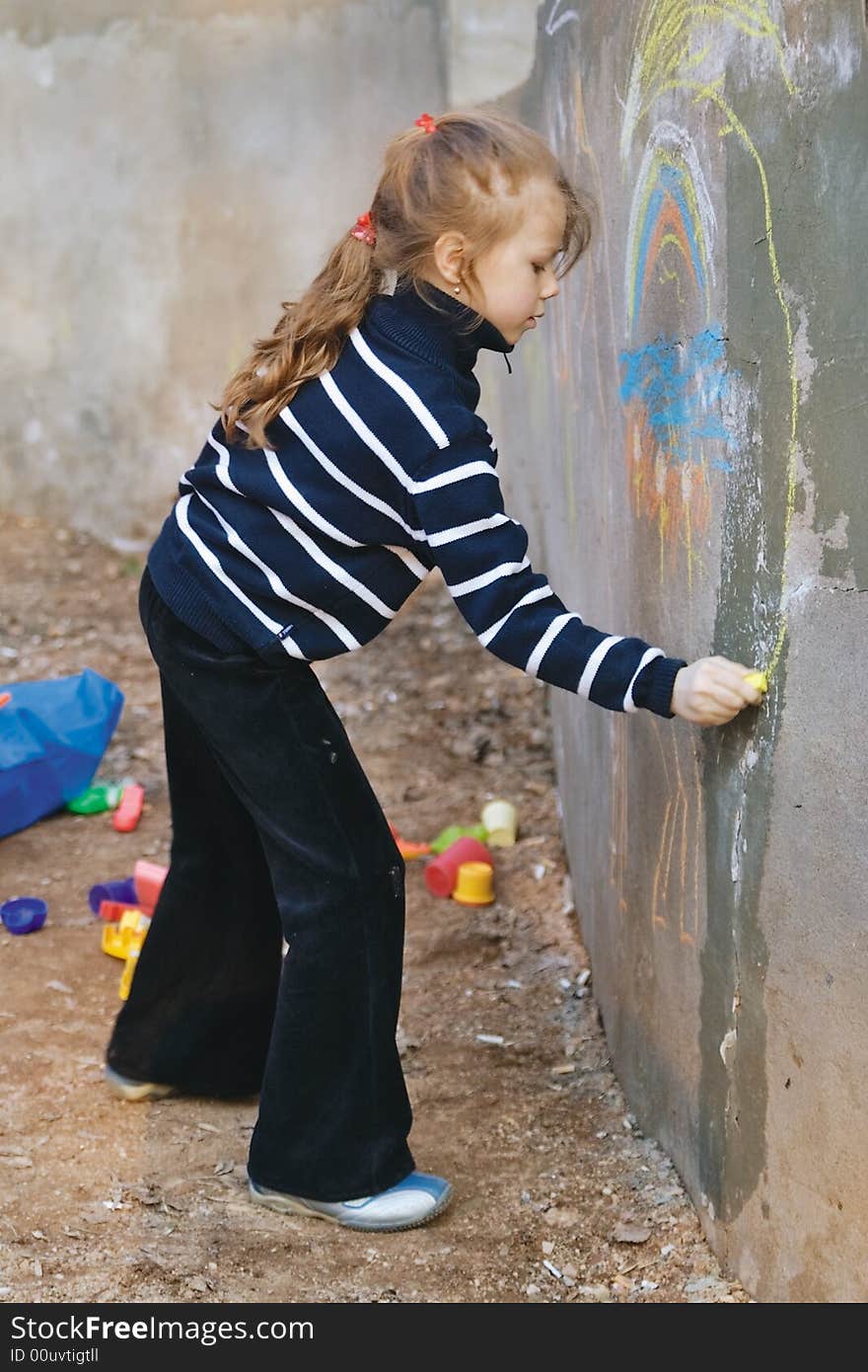 A girl-teenager draws a chalk on a grey wall. A girl-teenager draws a chalk on a grey wall