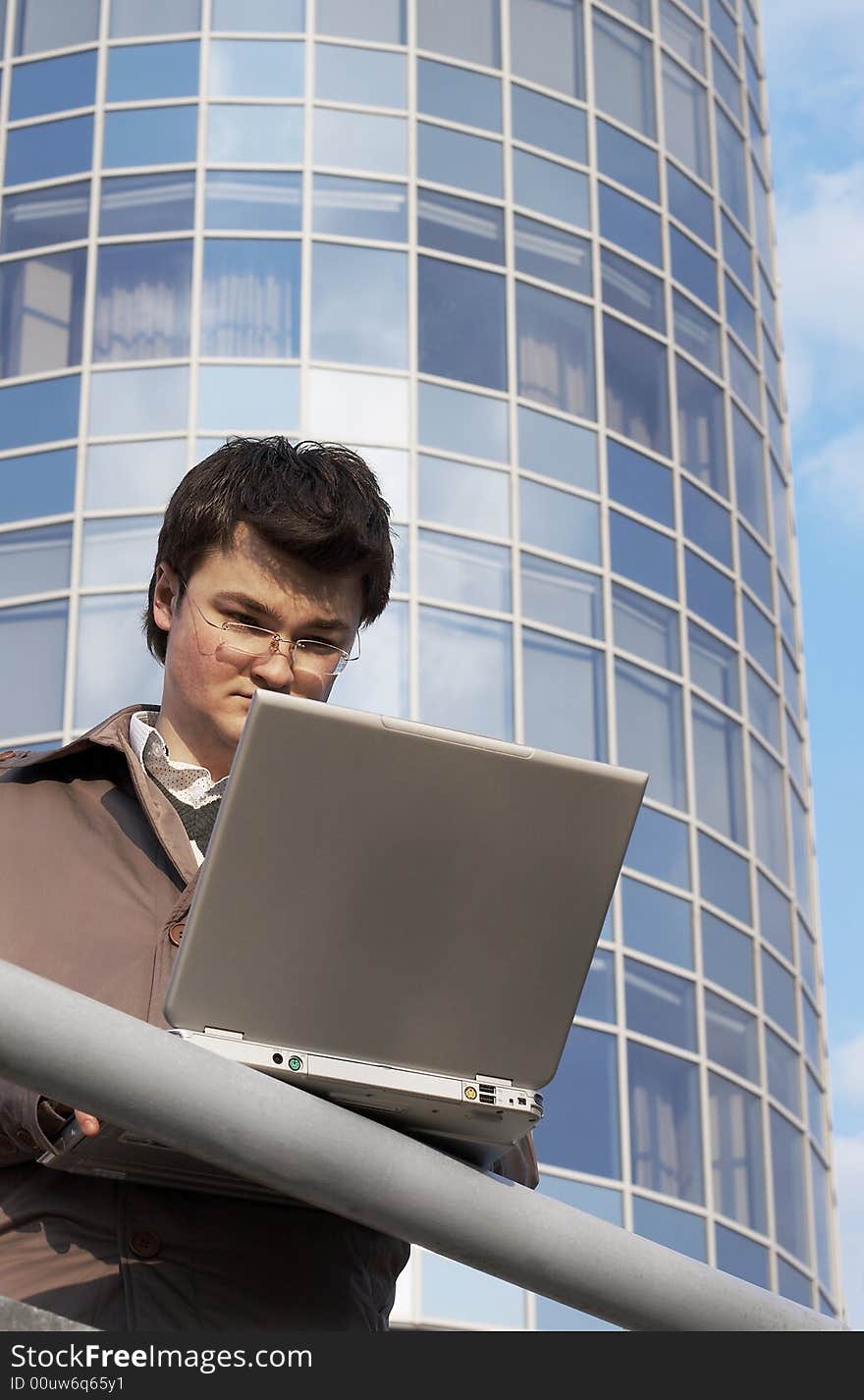 Young concentrated businessman with laptop on the building background