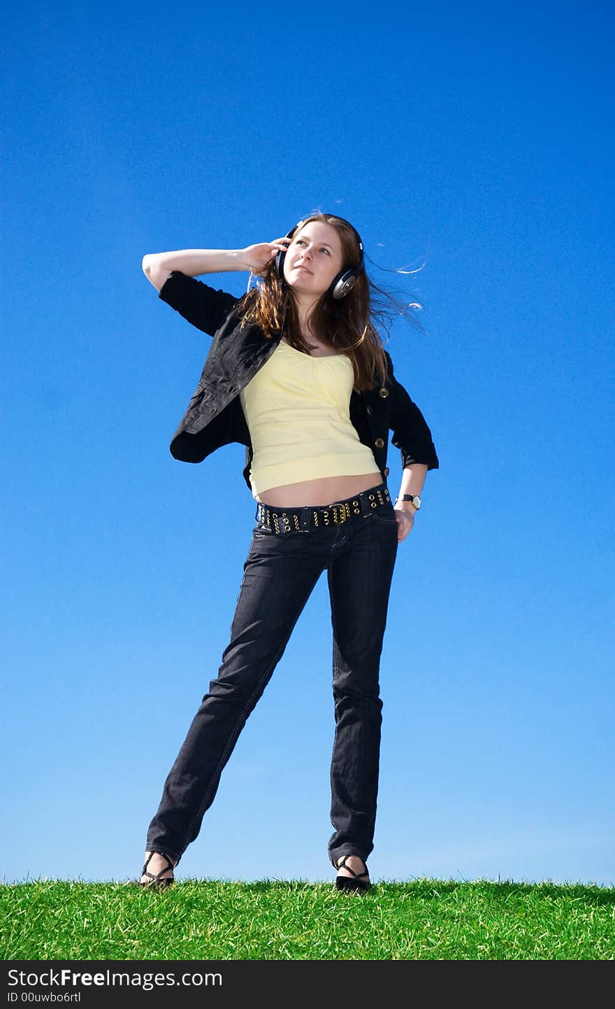 The young attractive girl with headphones on a background of the blue sky