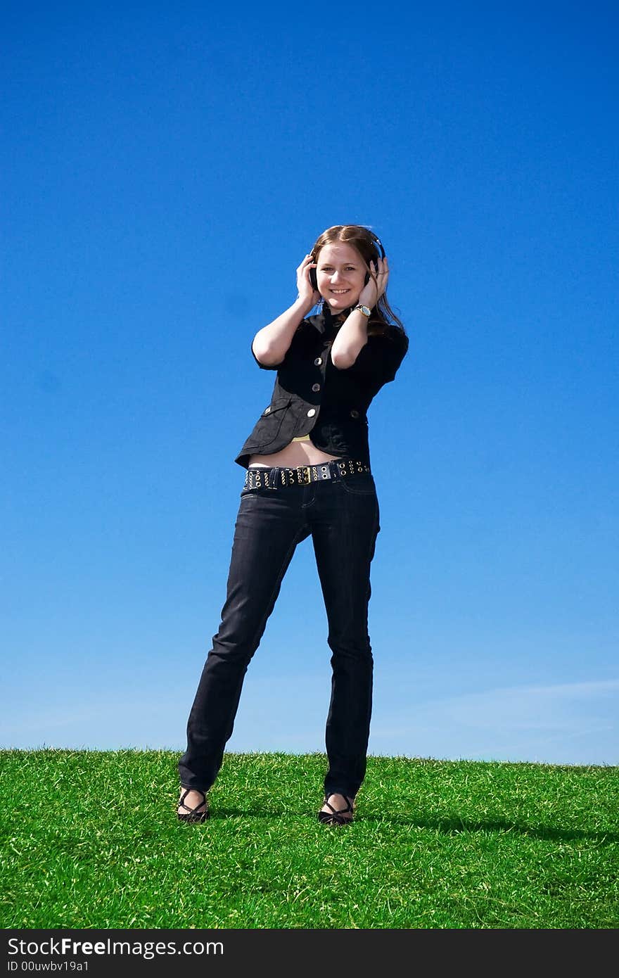 The young attractive girl with headphones on a background of the blue sky