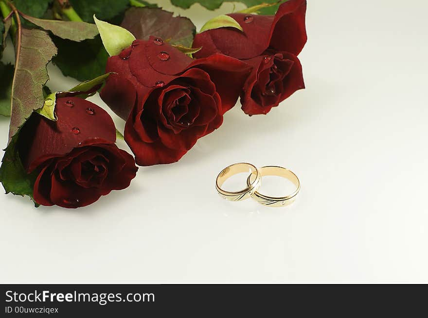Tree red roses with two wedding rings as a wedding background