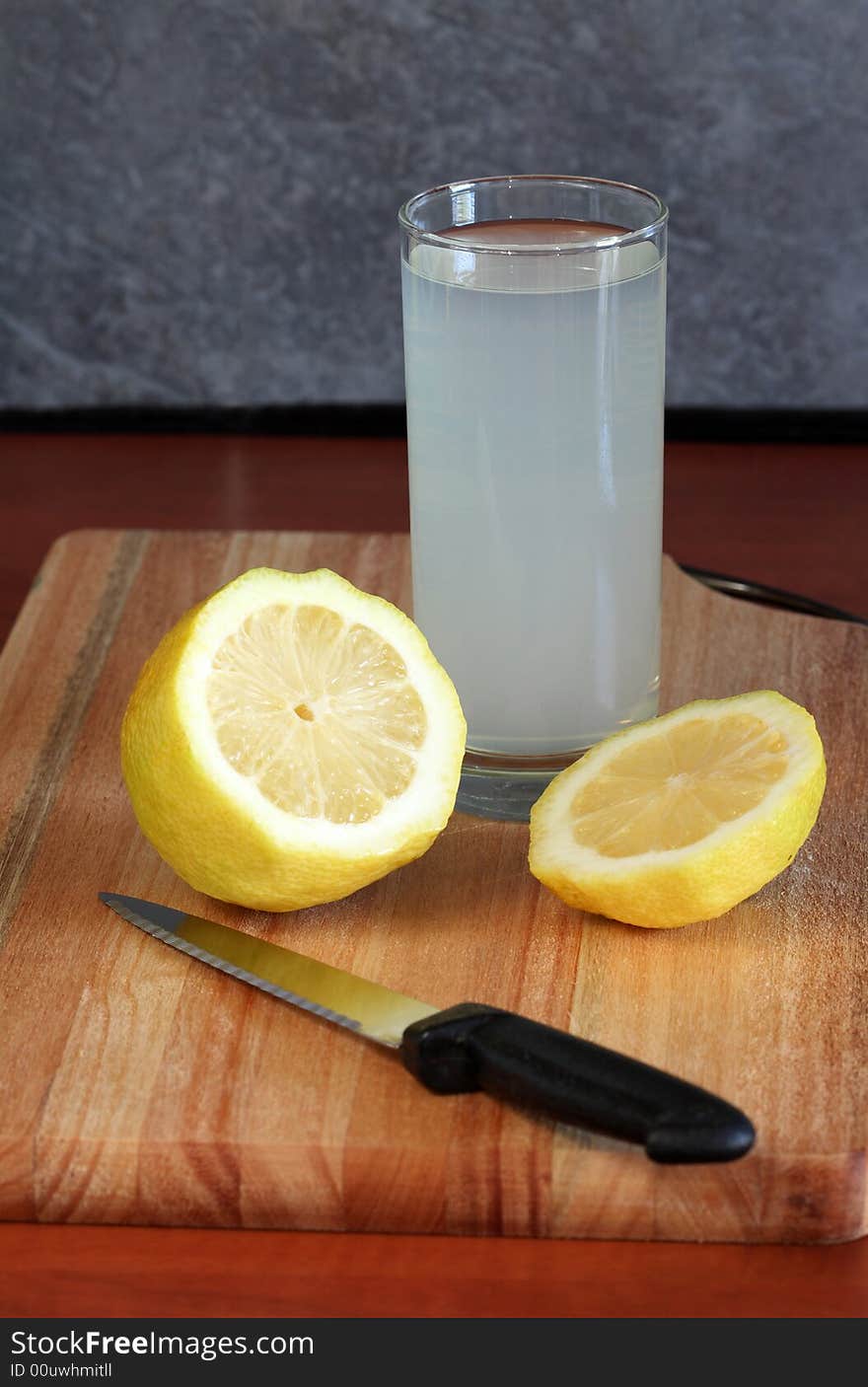 A glass of lemon on a cutting board with a piece of lemon and a knife. A glass of lemon on a cutting board with a piece of lemon and a knife.