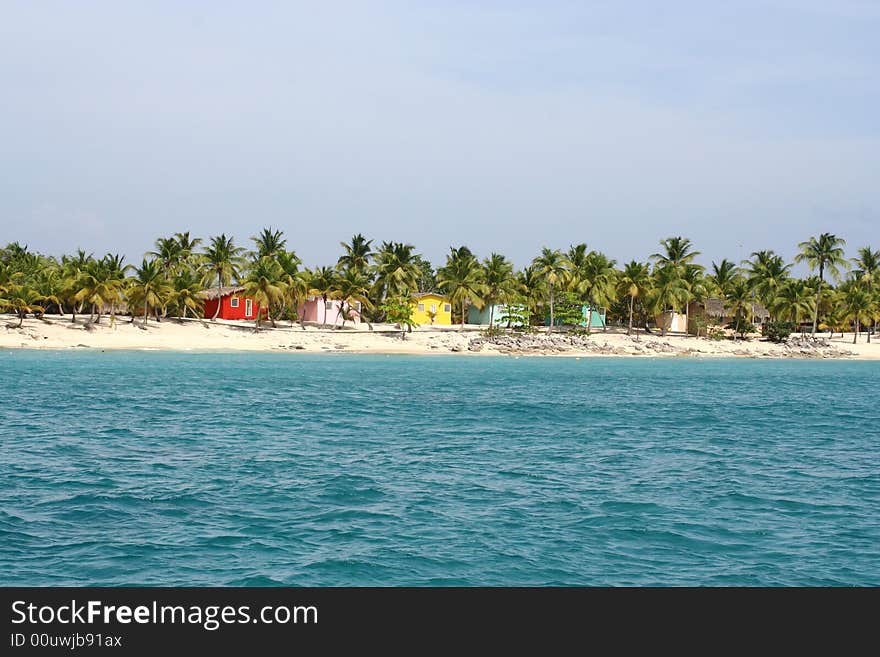 Caribbean white sand beach with palm trees andvibrantly coloured,wooden houses. Caribbean white sand beach with palm trees andvibrantly coloured,wooden houses.