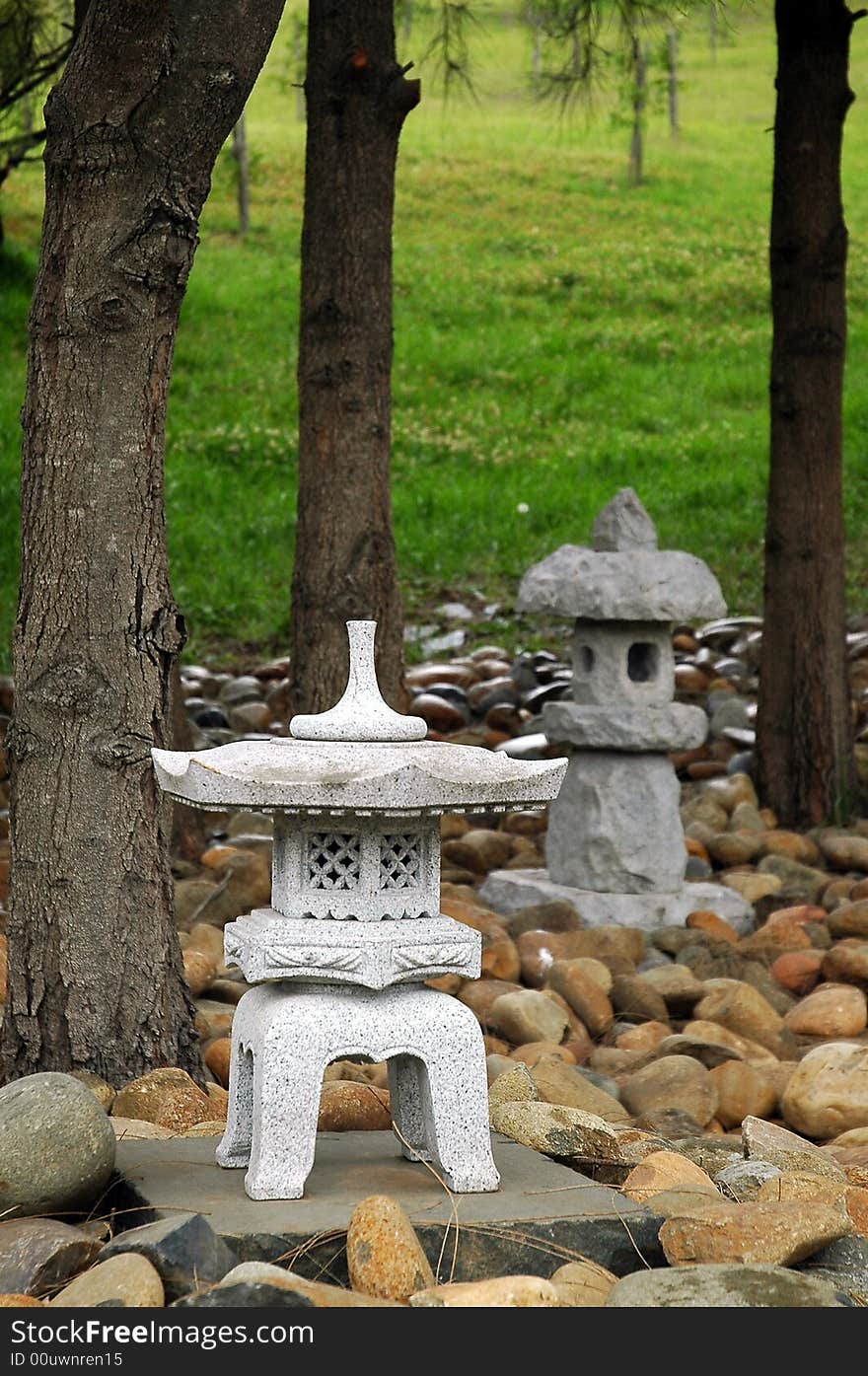 Small buddhist sculptures made of stone, small stones, green grass, and trees in background. Small buddhist sculptures made of stone, small stones, green grass, and trees in background