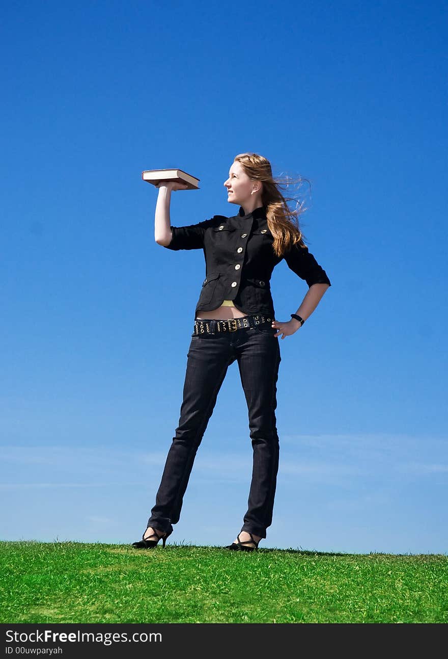 The young attractive student with the book on a background of the blue sky