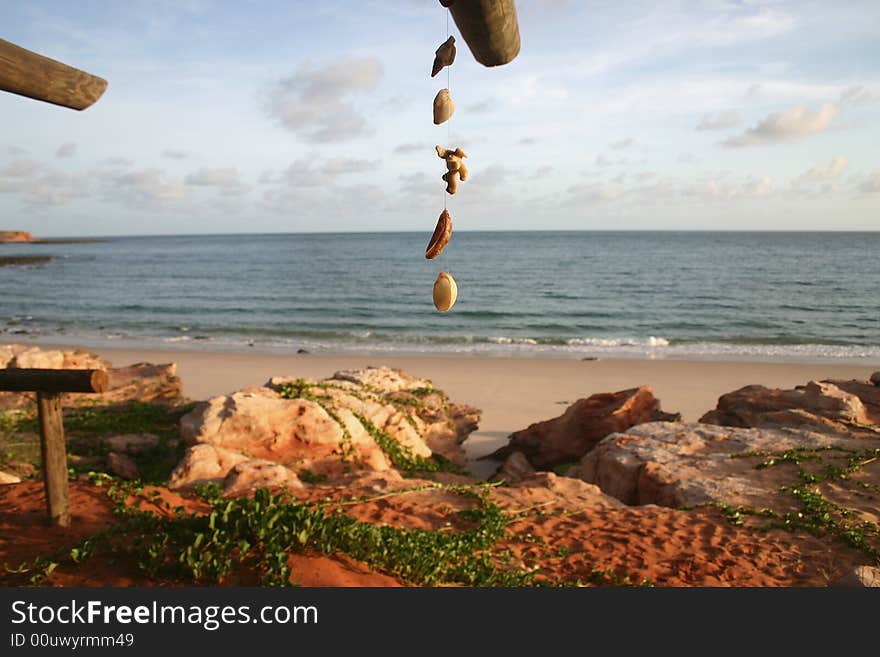 Hanging shells on a string with red rocks and sandy beach in background. Cape Leveque, The Kimberley. Australia