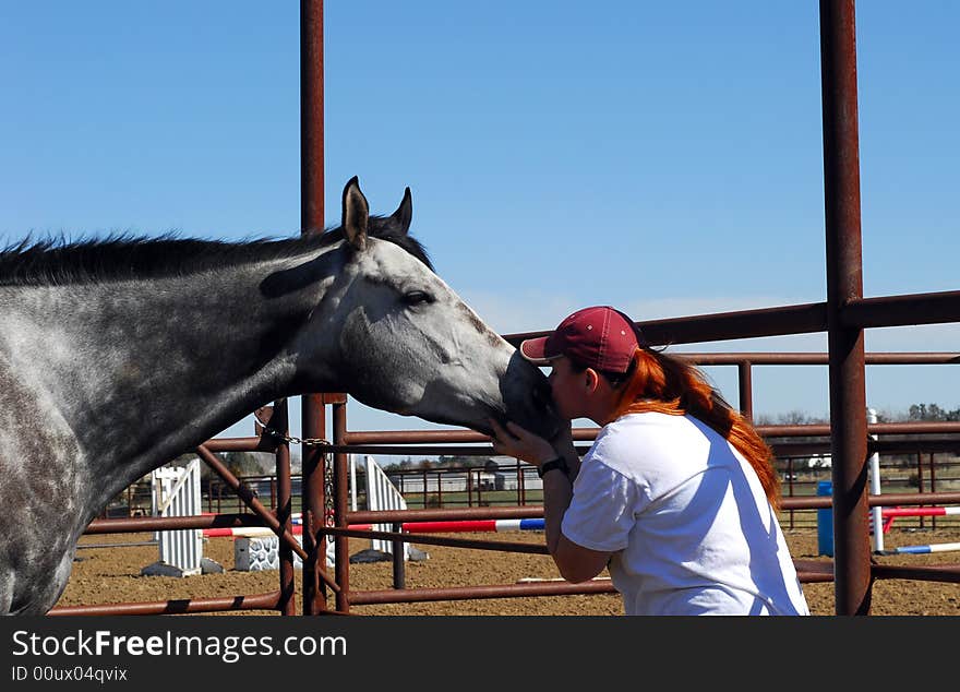 Red haired woman kissing grey horse on the nose. Red haired woman kissing grey horse on the nose.