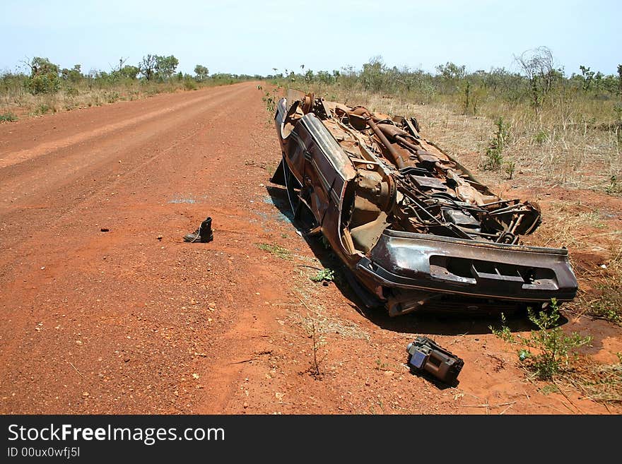 Australian red rural road with an overturned obsolete rusted car on the roadside. Tanami road, Western Australia. Australian red rural road with an overturned obsolete rusted car on the roadside. Tanami road, Western Australia