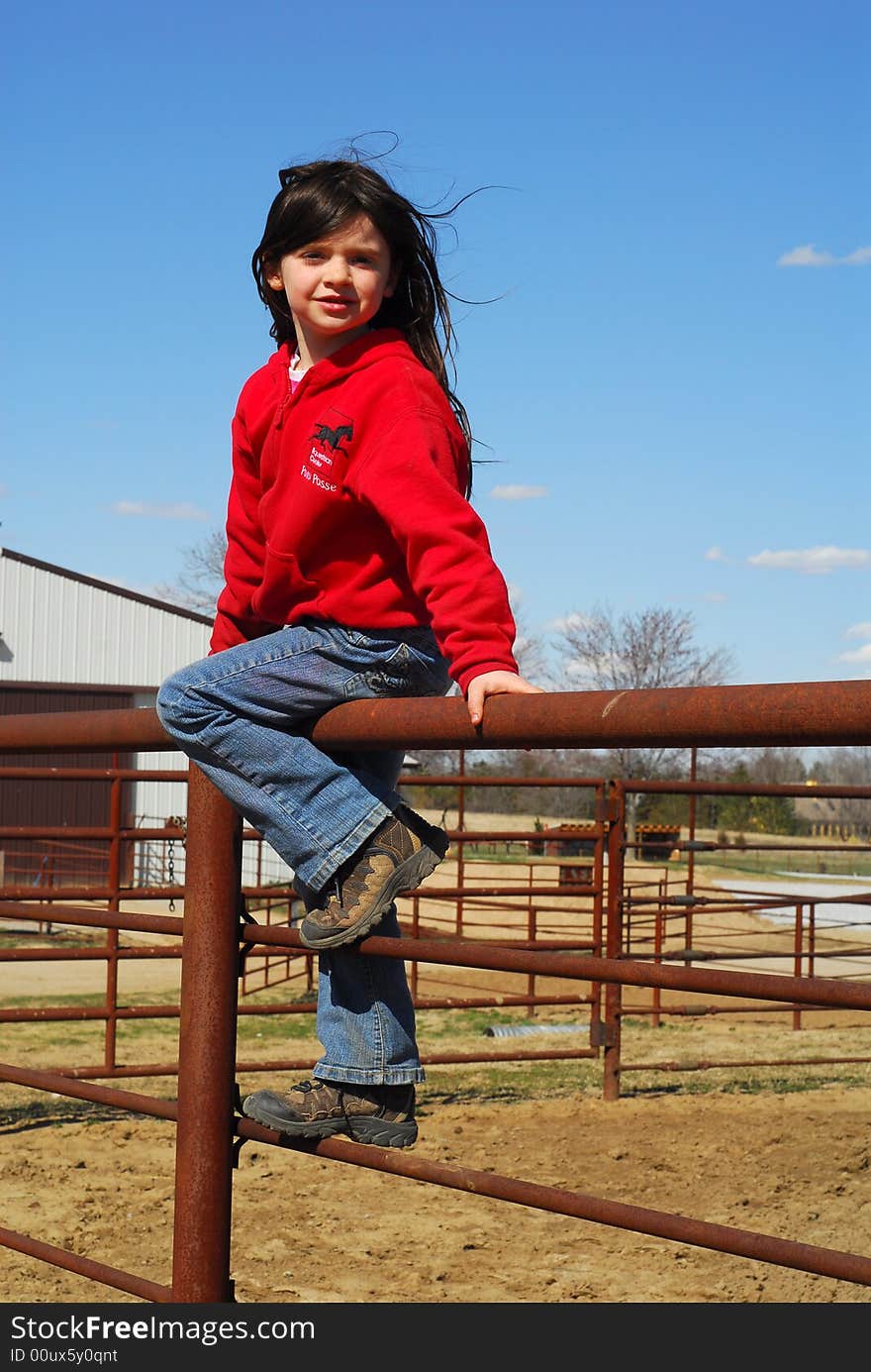 Pretty little girl sitting on metal fence by outdoor arena. Pretty little girl sitting on metal fence by outdoor arena.