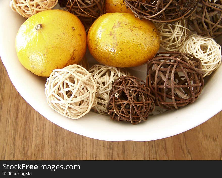 Image of honey tangerines and vine decorations mixed together in a white bowl on a wooden table.  Horizontal orientation.