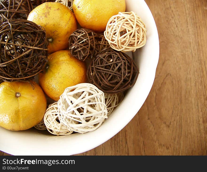 Image of honey tangerines and vine decorations mixed together in a white bowl on a wooden table, set to the left of the image.  Horizontal orientation.