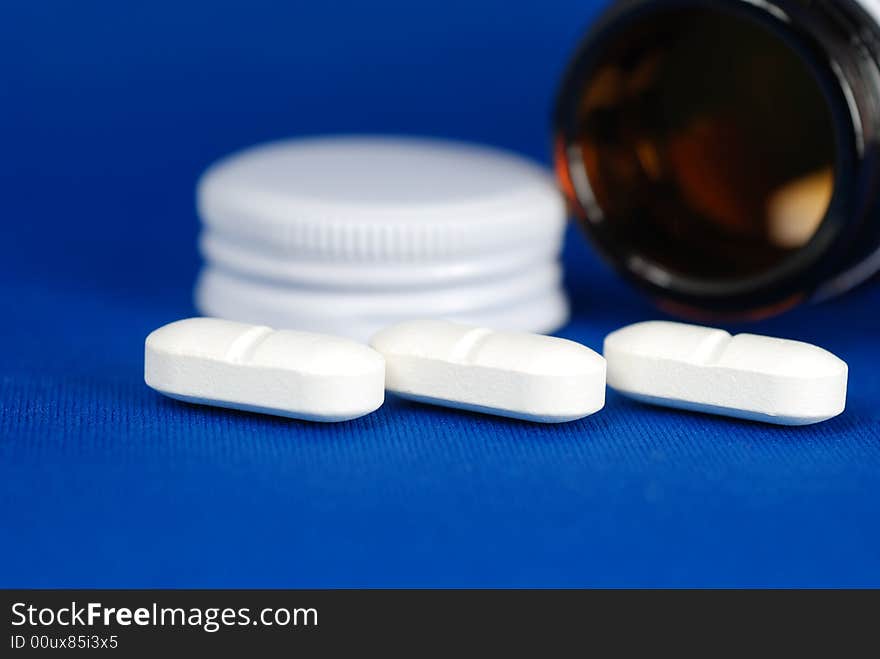 Close up to side by side pills , infront of a bottle and lid on blue background. Close up to side by side pills , infront of a bottle and lid on blue background