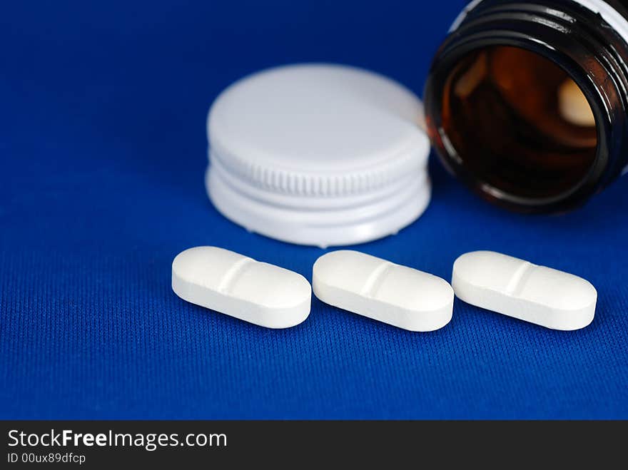 Close up to three pills infront of bottle and lid on blur background. Close up to three pills infront of bottle and lid on blur background