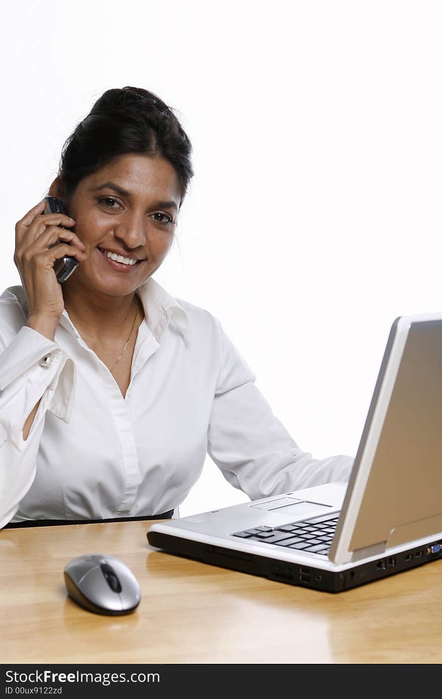 Indian business woman smiling on her cell phone while working at her laptop. Isolated against a white background. Indian business woman smiling on her cell phone while working at her laptop. Isolated against a white background