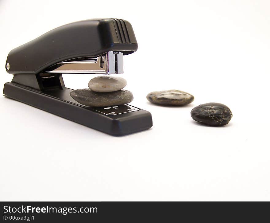 Image of a black stapler, about to staple two rocks together, with other rocks nearby.  Horizontal orientation. Image of a black stapler, about to staple two rocks together, with other rocks nearby.  Horizontal orientation.