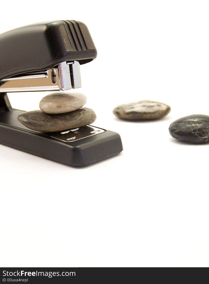 Image of a black stapler about to staple two stones together.  Other stones are nearby.  Vertical orientation. Image of a black stapler about to staple two stones together.  Other stones are nearby.  Vertical orientation.