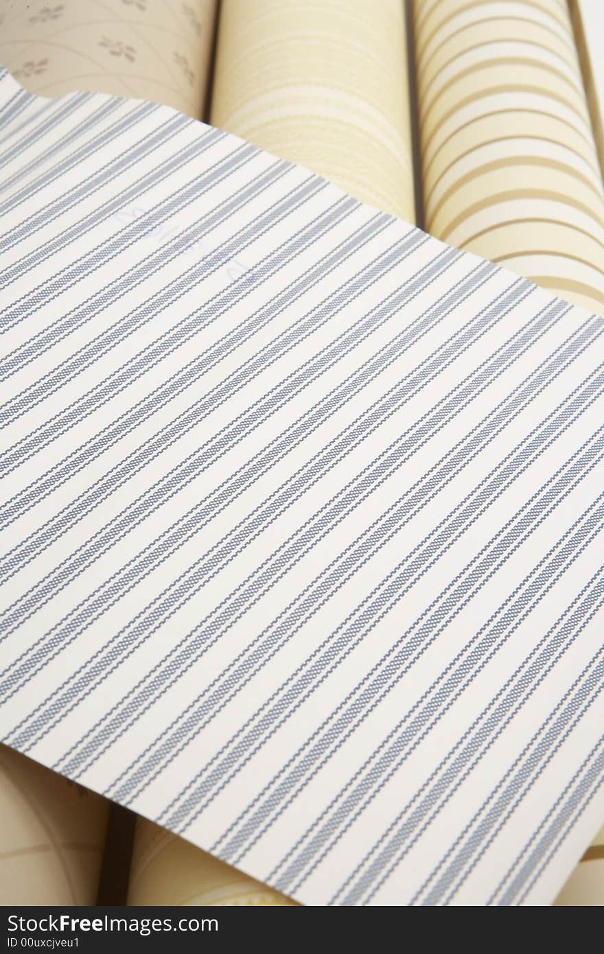 Close up of blue striped wall paper swatch on top of three beige wall paper rolls. Close up of blue striped wall paper swatch on top of three beige wall paper rolls.