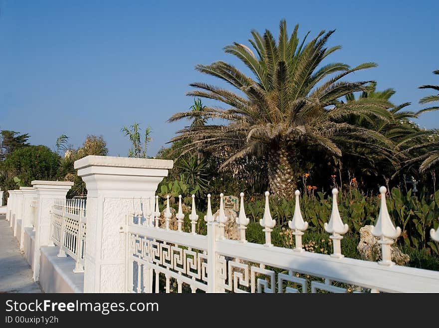 Greece motifs white fence near palm tree garden. Greece motifs white fence near palm tree garden