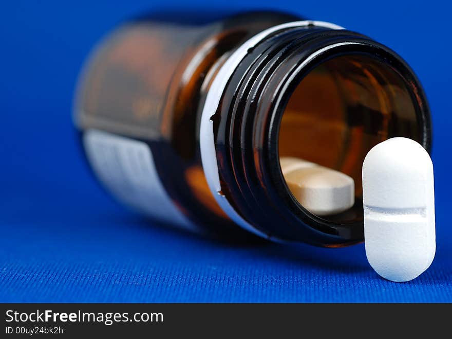 Close up to a pill placed on the right corner of frame together with open bottle of medicine on blue background