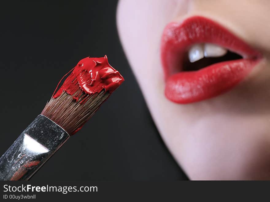 A brush with paint and red lips in background