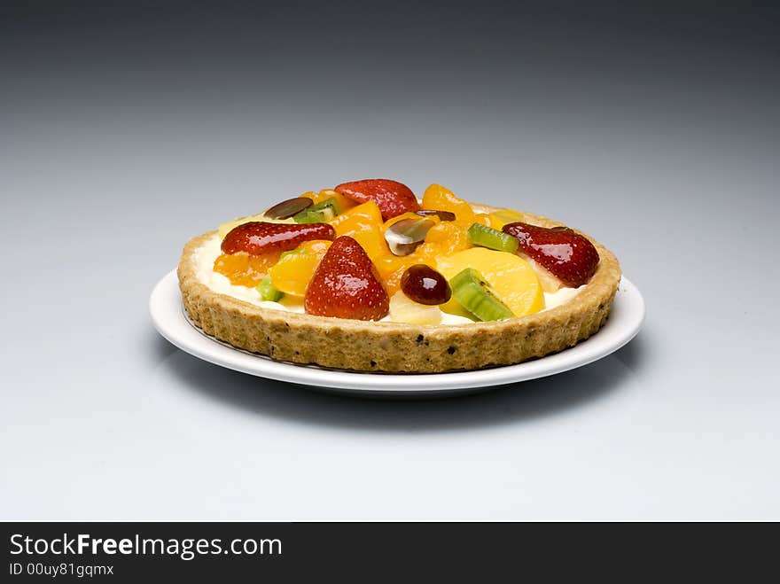 A fruit pie in a plastic transparent box on a gray to white background