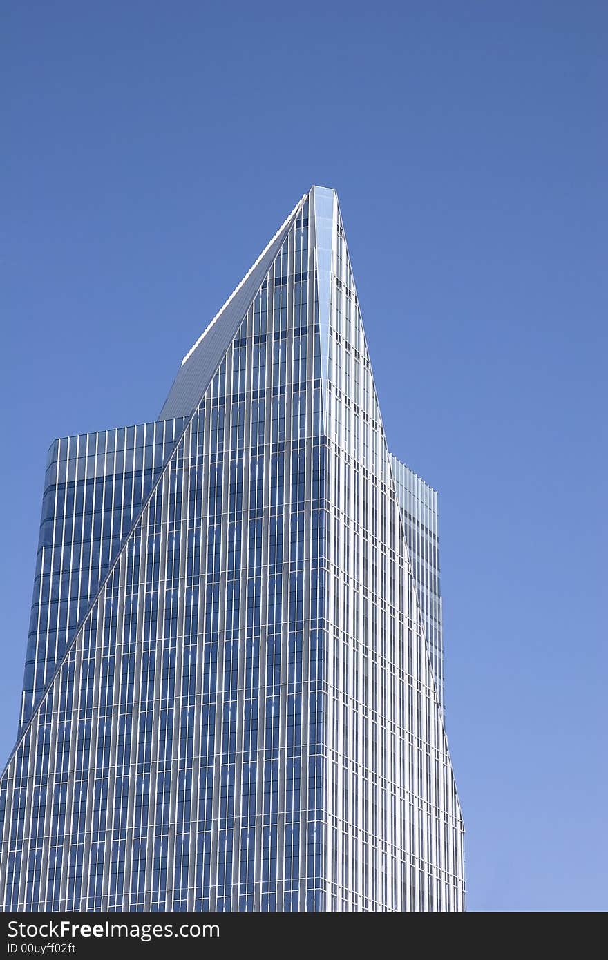 A modern blue glass skyscraper with a pyramid top against a blue sky. A modern blue glass skyscraper with a pyramid top against a blue sky