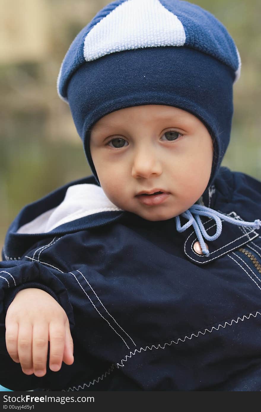 The portrait of a fullface of the little boy dressed in a dark blue jacket and blue takes