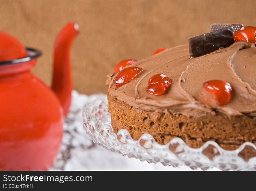 Chocolate cake with cherries and a red tea pot. Chocolate cake with cherries and a red tea pot