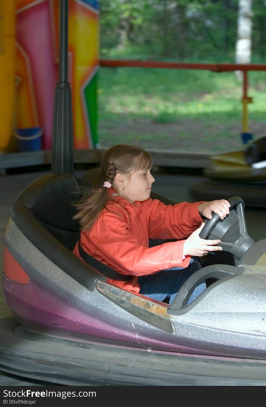 The girl-teenager goes on the toy car in park of entertainments