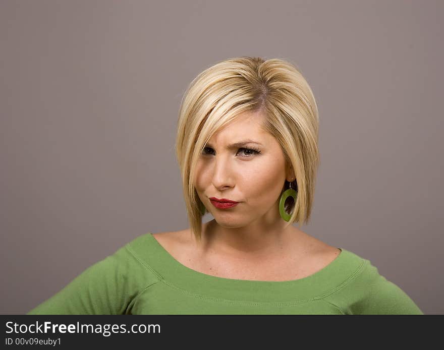 A blonde in green blouse on grey background with a stern or disapproving look. A blonde in green blouse on grey background with a stern or disapproving look