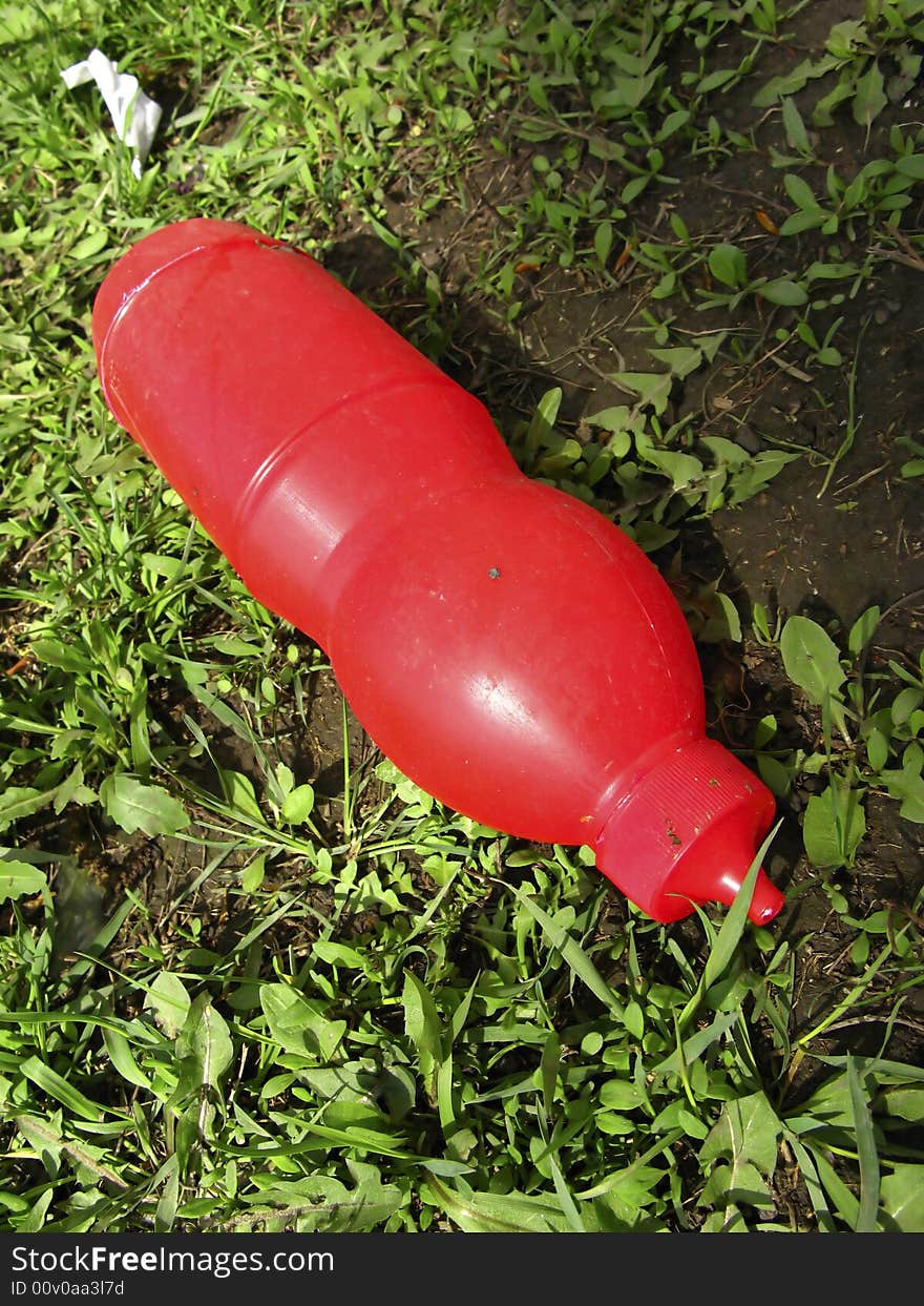 Thrown plastic bottle of red color on  background of  grass