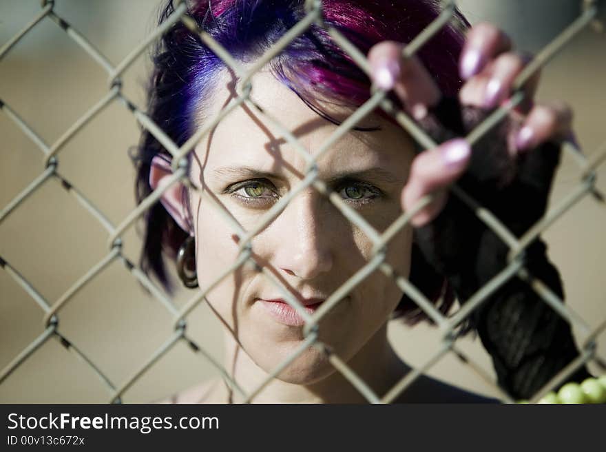 Young woman with colorful hair behind a chain link fence. Young woman with colorful hair behind a chain link fence