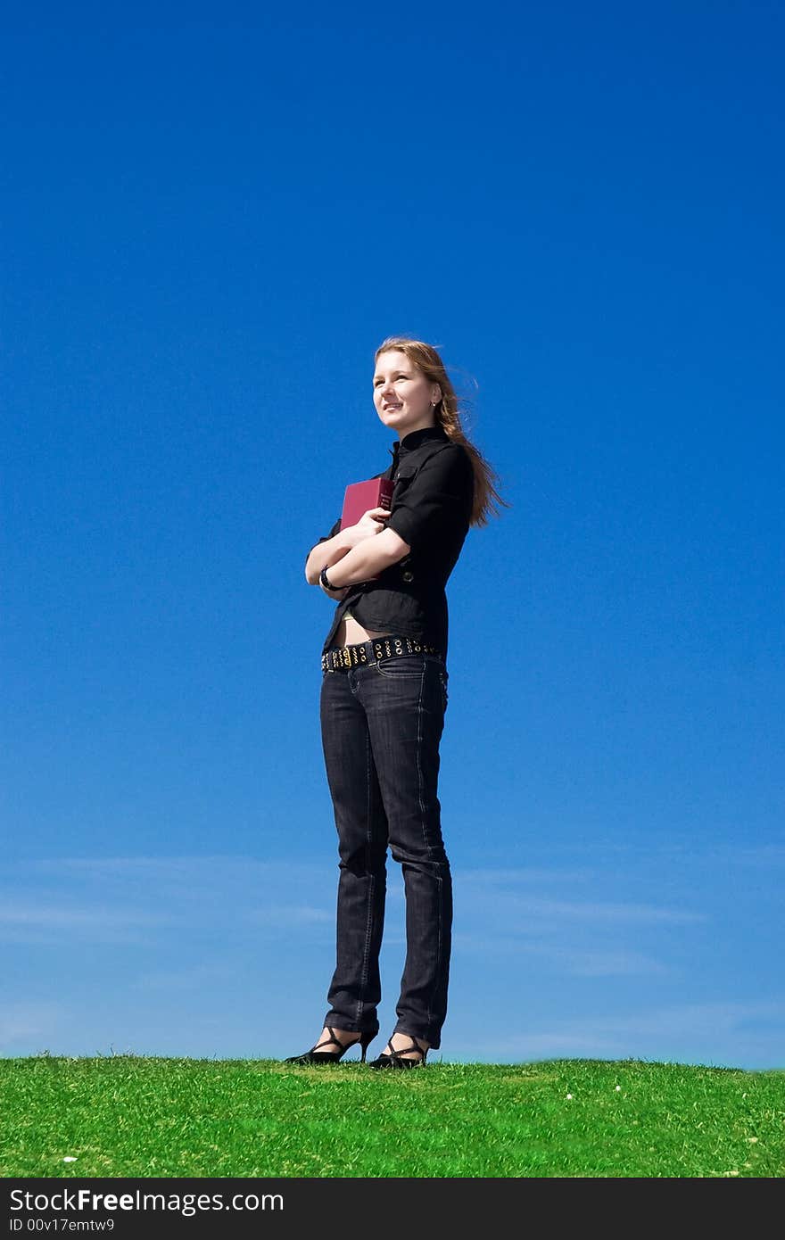 The young attractive student with the book on a background of the blue sky