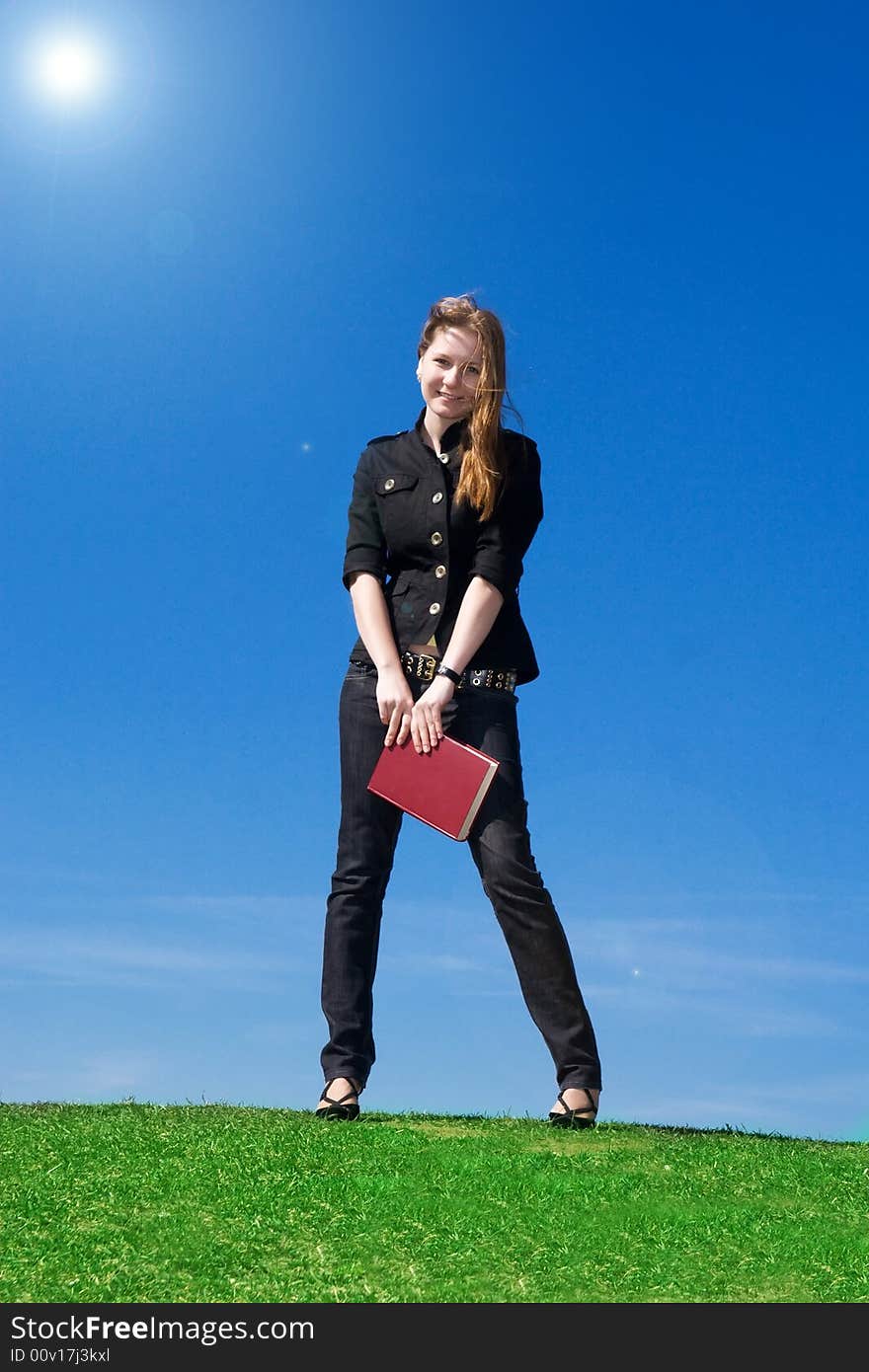 The young attractive student with the book on a background of the blue sky