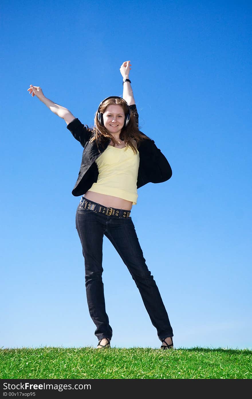 The young attractive girl with headphones on a background of the blue sky