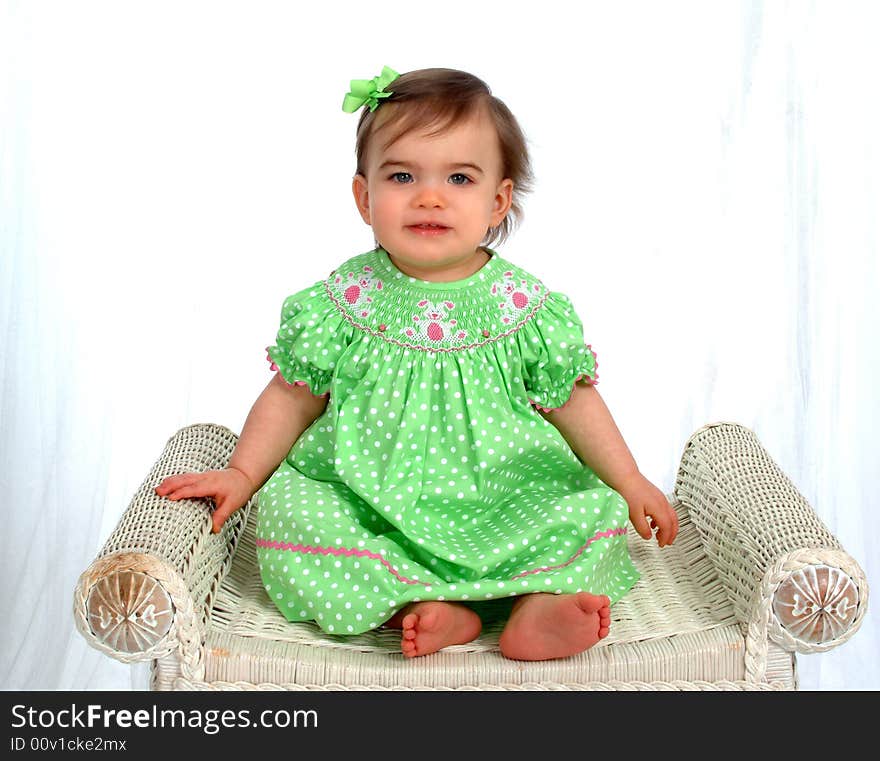 Baby girl in green sitting on bench in front of white background. Baby girl in green sitting on bench in front of white background