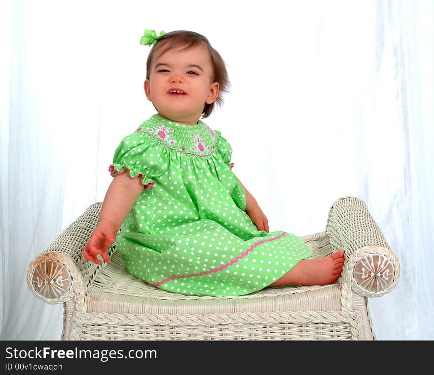 Funny baby girl in green polka dot dress sitting on bench in front of white background. Funny baby girl in green polka dot dress sitting on bench in front of white background