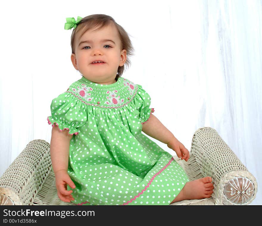 Baby girl in green polka dot dress sitting on bench in front of white background. Baby girl in green polka dot dress sitting on bench in front of white background