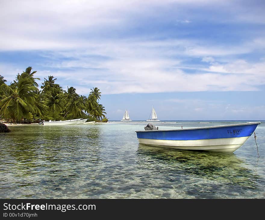 Boat anchored in beautiful tropical cove with palm trees and sailboats in the background. Boat anchored in beautiful tropical cove with palm trees and sailboats in the background.