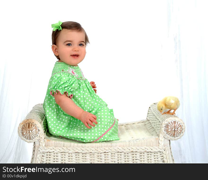 Baby girl on wicker bench looking at camera with chick perched on bench in front of white background. Baby girl on wicker bench looking at camera with chick perched on bench in front of white background