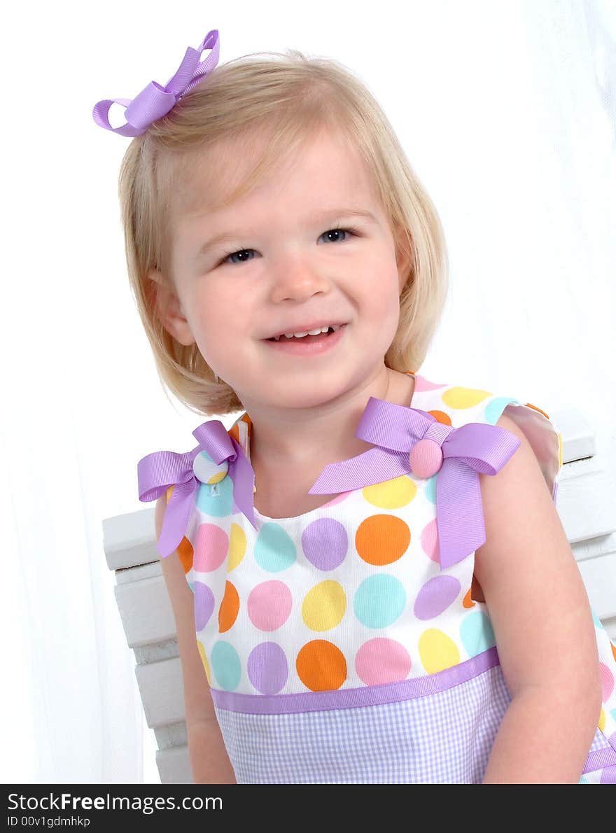 Closeup of smiling blond girl in colorful polka dot dress in front of white background. Closeup of smiling blond girl in colorful polka dot dress in front of white background