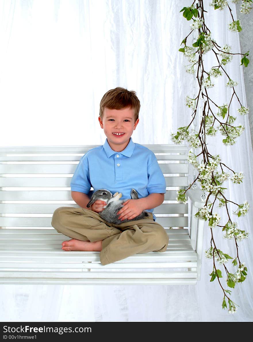 Boy in blue sitting with bunny on swing in front of white background. Boy in blue sitting with bunny on swing in front of white background