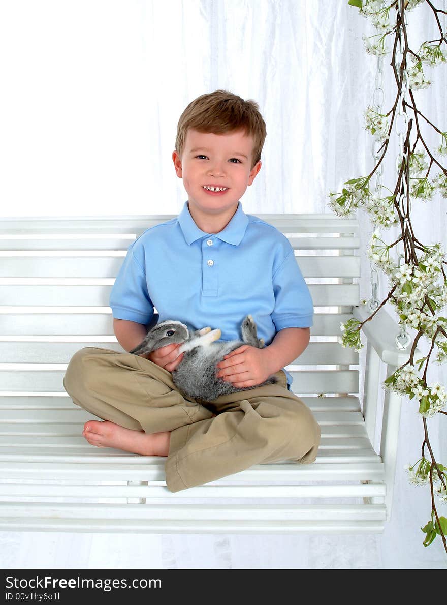 Boy in blue sitting with bunny on swing in front of white background. Boy in blue sitting with bunny on swing in front of white background