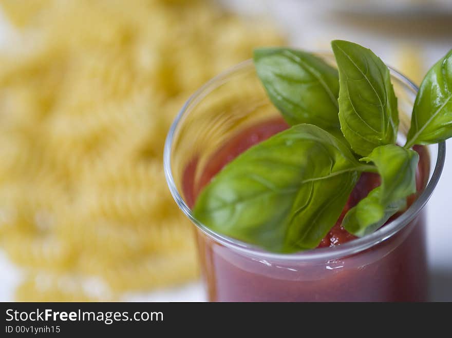 Bowl with tomato sauce and basil and pasta on the background