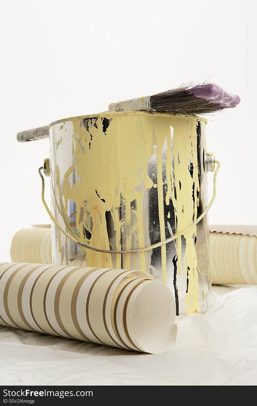 Brush dipped in purple paint on top of a can of yellow paint with two wall paper samples on either side. Brush dipped in purple paint on top of a can of yellow paint with two wall paper samples on either side.