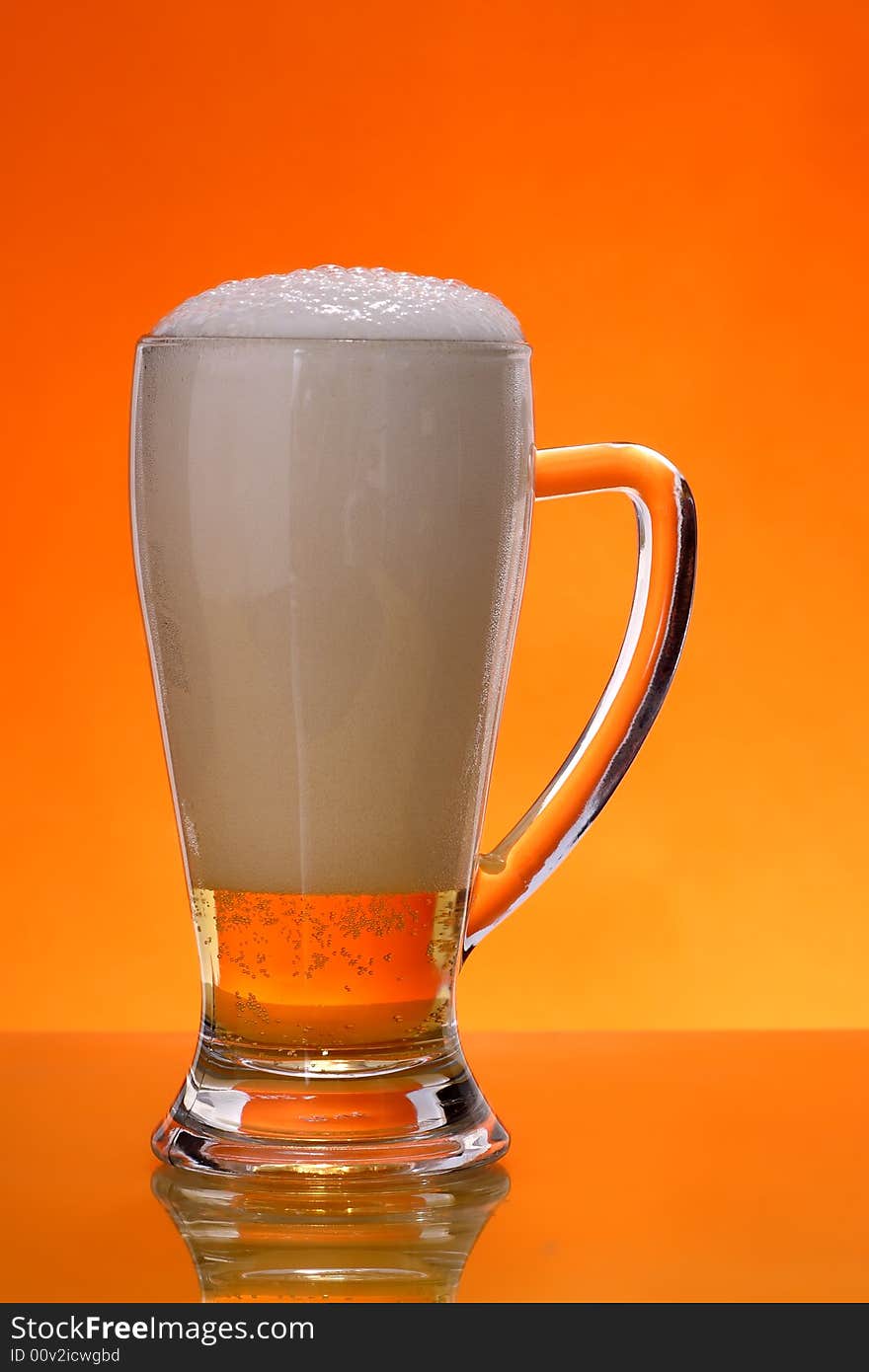 Glass of beer with froth over orange background